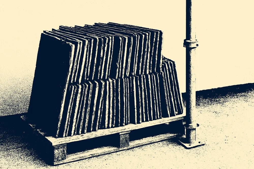 Reclaimed slates stacked on edge on a pallet beside a scaffold pole — slate roofing, Hobart. Illustrative example.